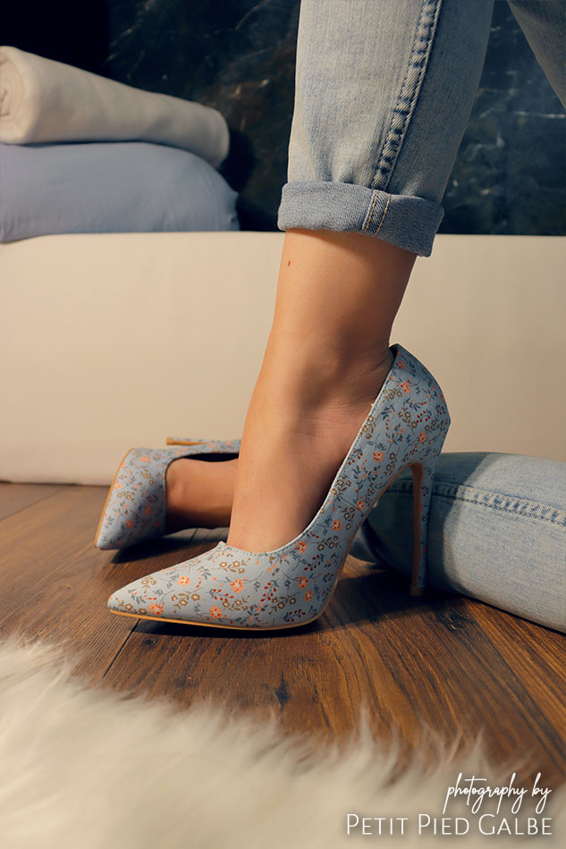 Close-up on a girl sitting on the wooden floor in blue high heels. Girl is wearing pants that match the color of the shoes.