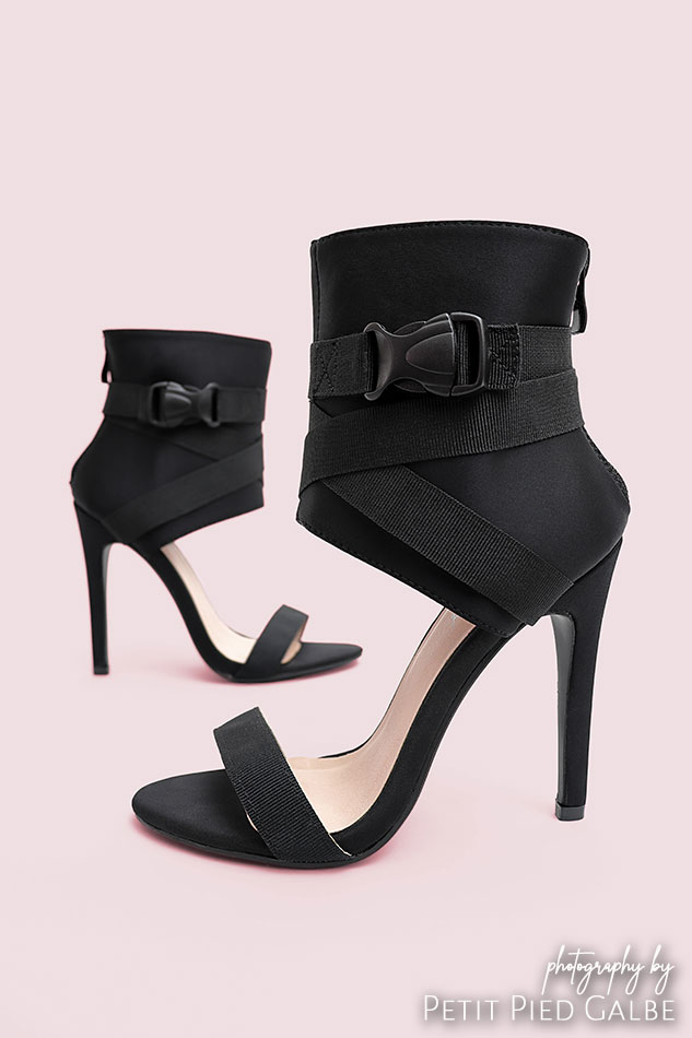 Black high heeled sandals with a high ankle upper shown from sides on pink background.