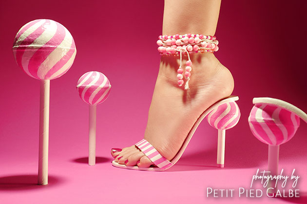 Close-up on a model wearing unique shoes and anklet jewelry. Next to her stands lollipops. Conceptual fashion for women.