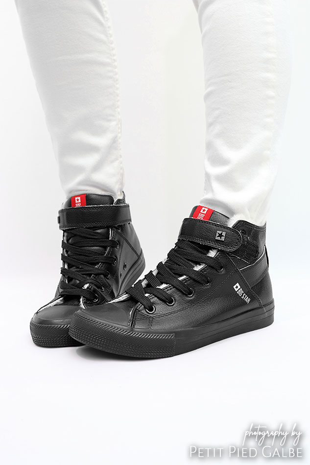 Professional photoshoot with model in a studio. Close-up on black high-top sneakers shown on a girl.