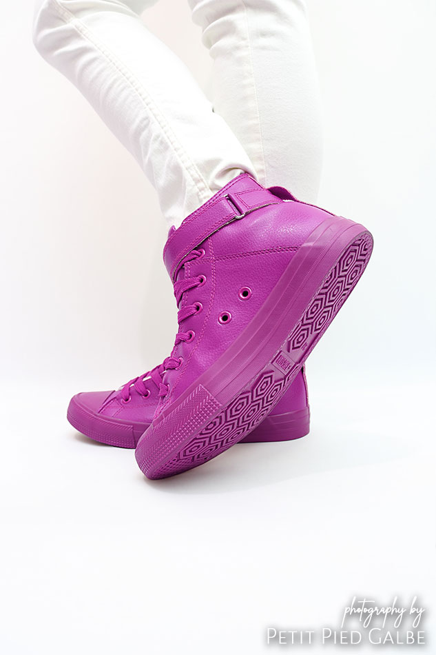 Girl is standing in photography studio in purple sport shoes and poses to the camera.