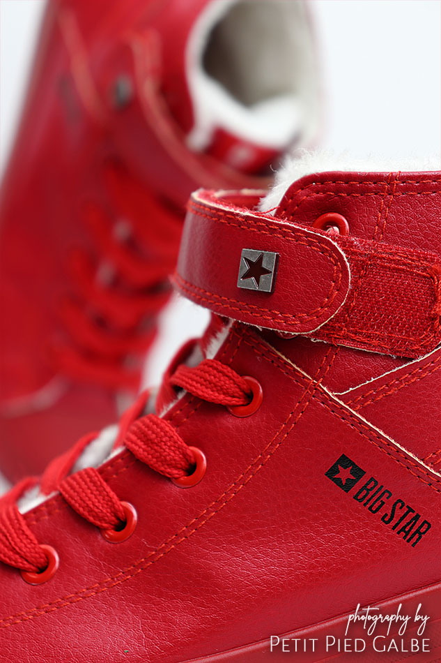 High top red sneaker on white background, close-up on velcro closure and laces.