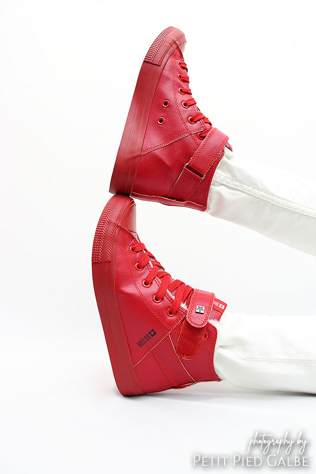 Professional model wearing high top red sneakers. Girl is sitting on the floor in photography studio, close-up on the shoes.