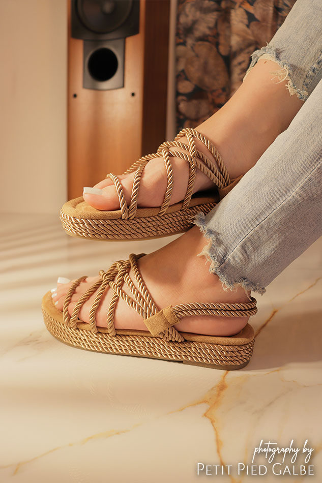 Professional model sitting on the marble floor showcasing summer lace sandals to the camera.