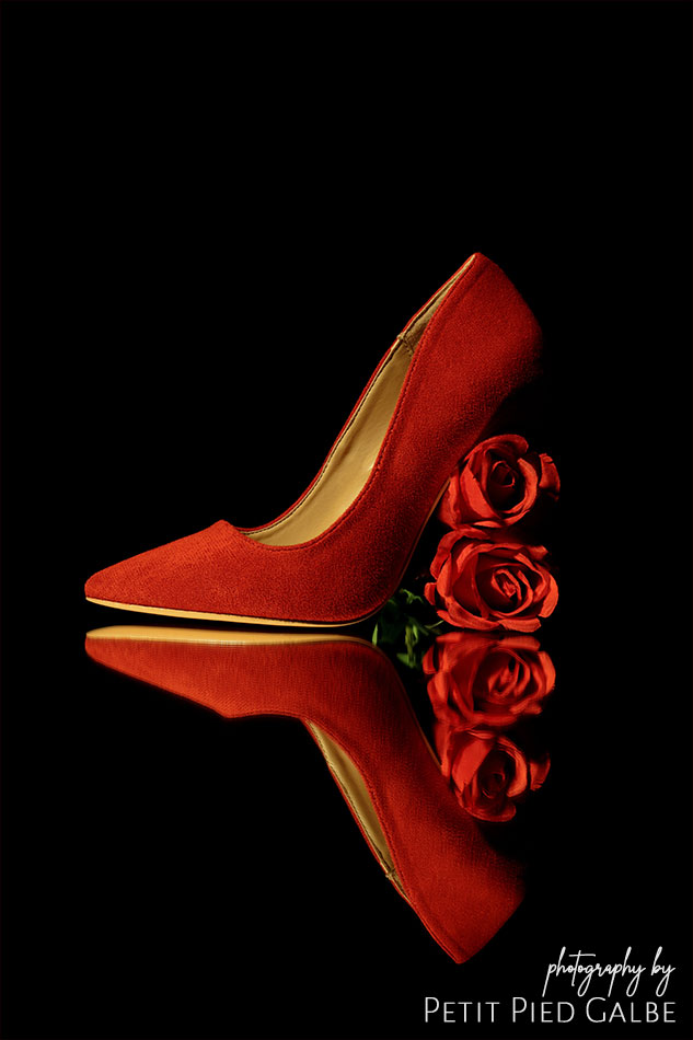 Red high heel with stiletto made from roses, standing on a mirror floor in dark scenario.