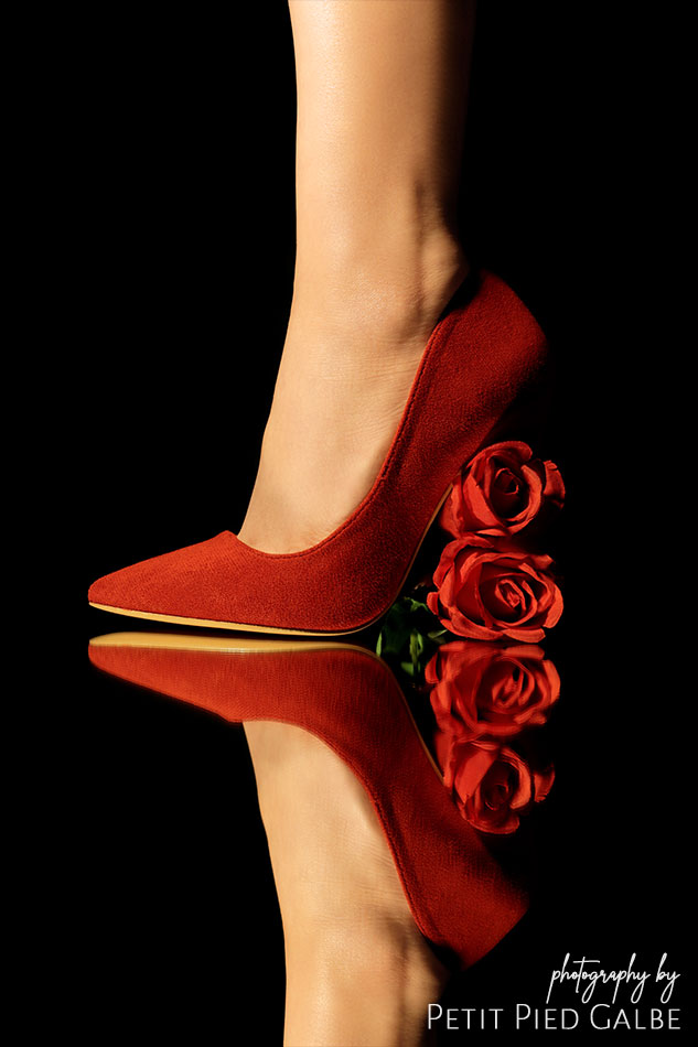 Model in red high heels with roses stiletto standing on a mirror floor. Close-up on a shoe.