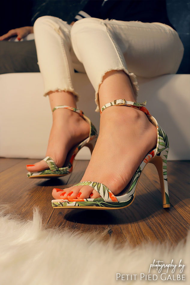 Atractive woman in heeled sandals with plant flower pattern sitting on a sofa. Girl is showing shoes close to the camera.