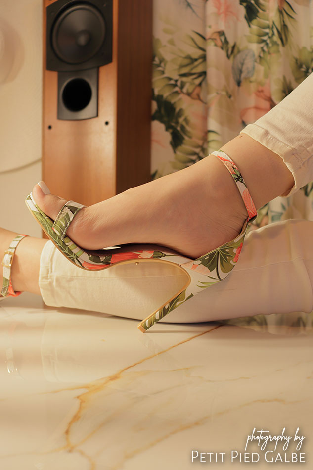 Model sitting on a floor in a plant pattern heeled sandals. Warm and intensive sunny light.