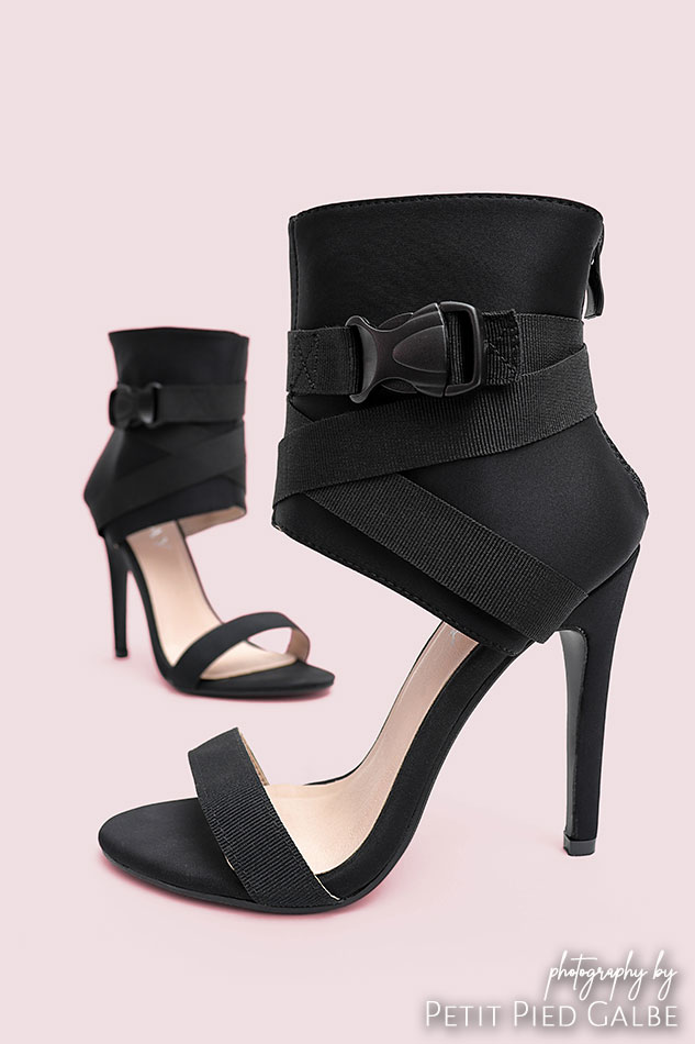 Shoes shown on a solid background, side view of strappy sandals on high heel.